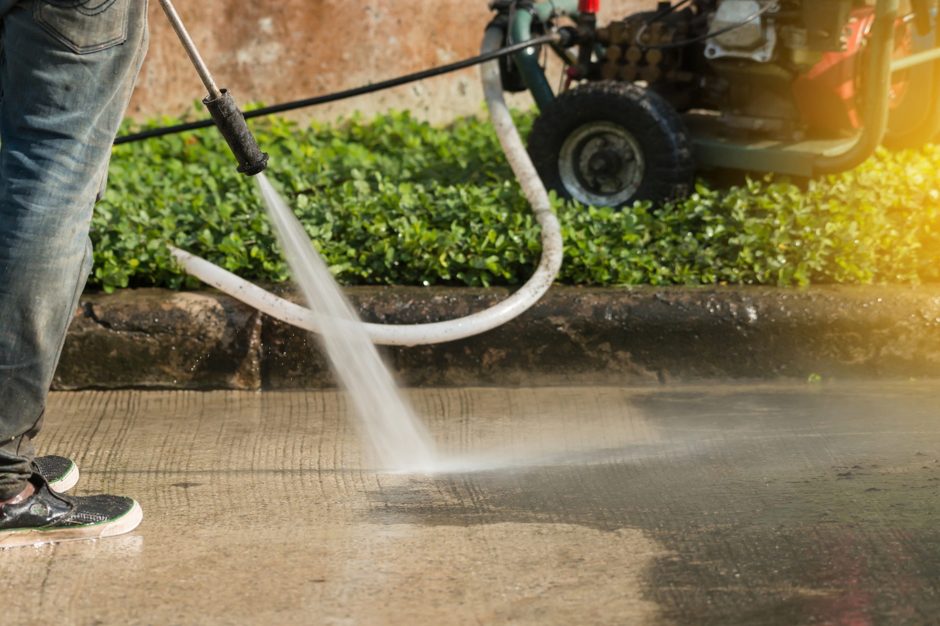 A homeowner using a pressure washer to clean his concrete driveway.